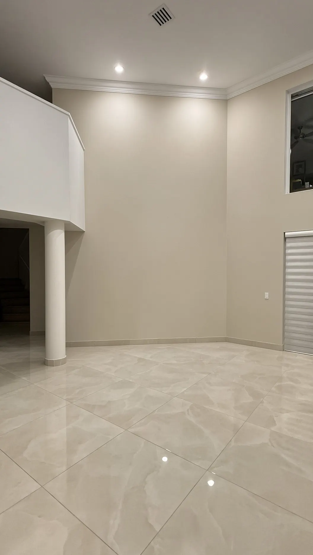 Pared de doble altura del salón antes: pintura beige lisa entre una columna y una ventana, sin nada