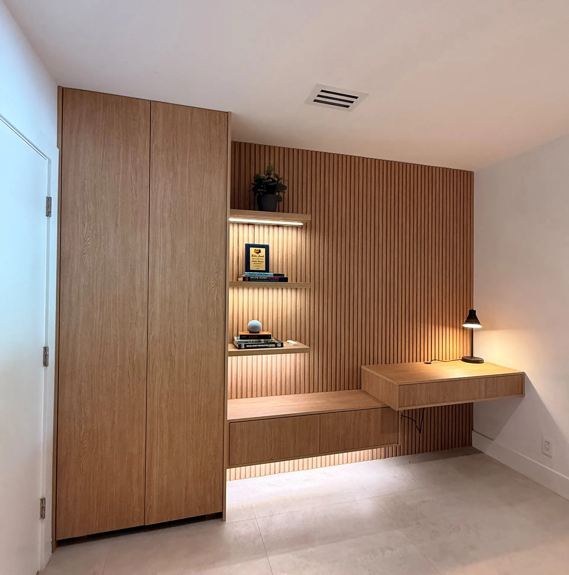 La misma pared después: un closet de roble del piso al techo, panelado de listones con nichos iluminados y un escritorio flotante