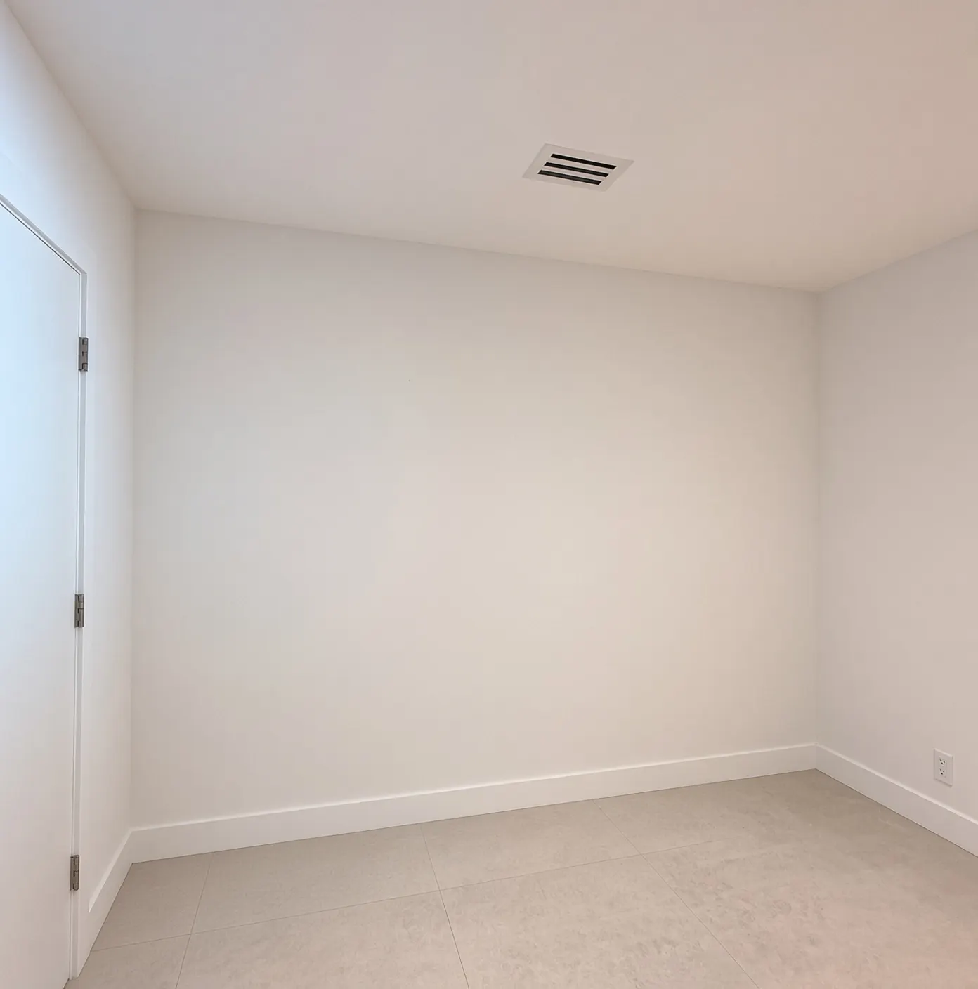 El cuarto antes: una pared blanca vacía junto a la puerta, con la rejilla del aire y piso de porcelanato