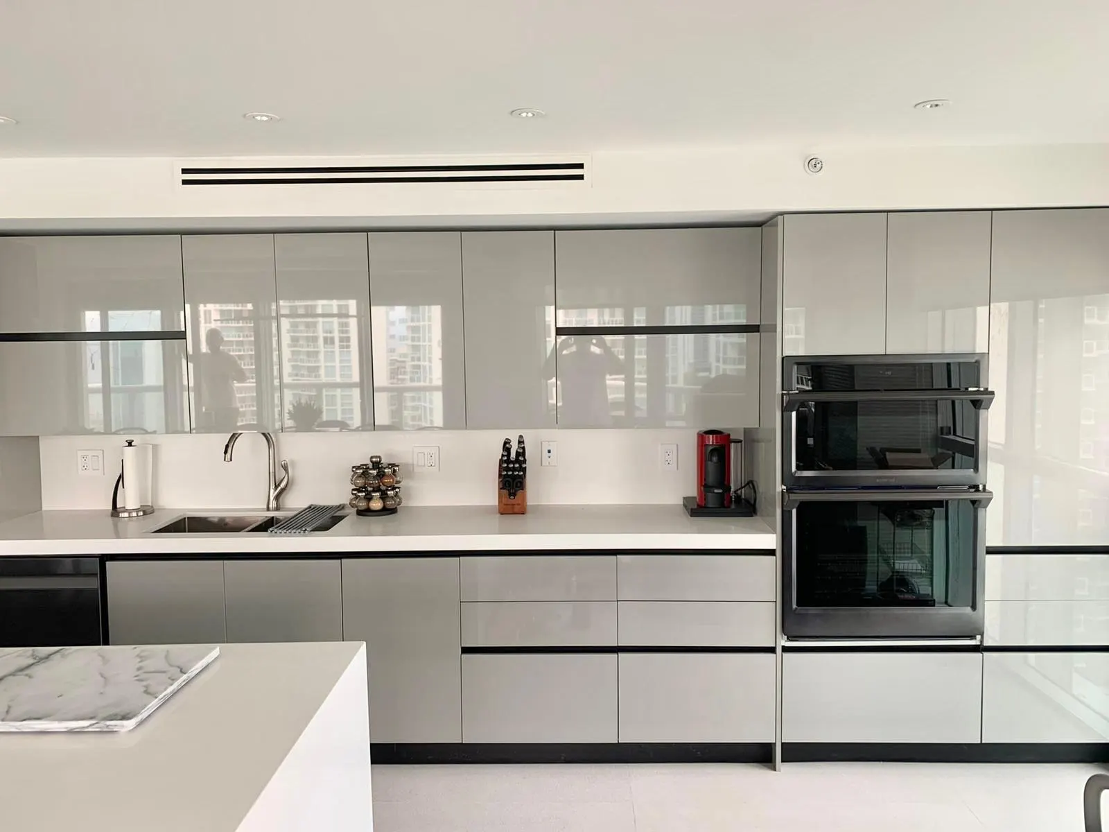 Cocina moderna con muebles grises de alto brillo sin tiradores, tope de cuarzo blanco, horno doble empotrado e isla con tope de mármol